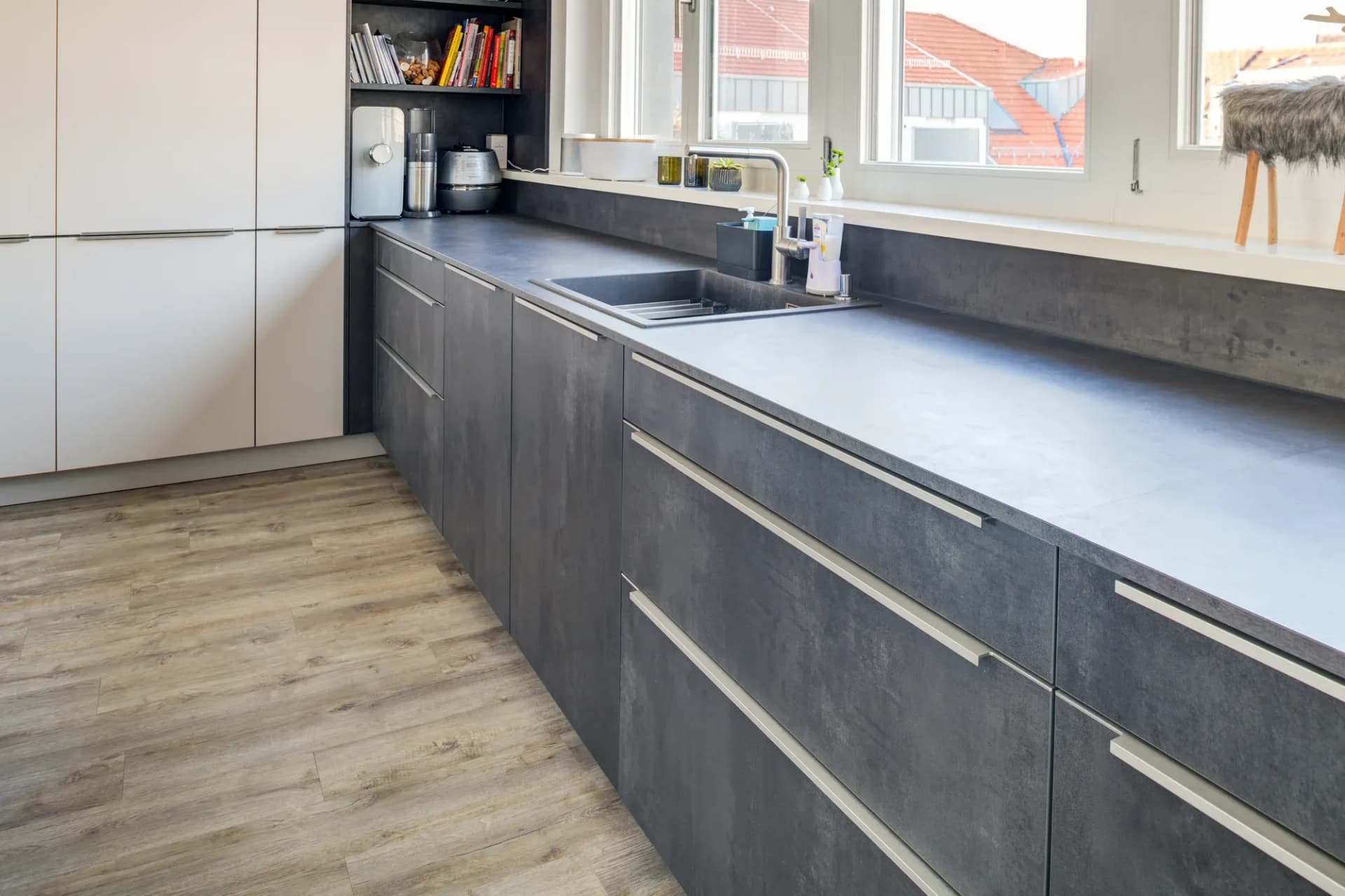 Niedrige Schrankzeile in Beton-Optik mit grauer Arbeitsplatte entlang der Fensterfront, Blick über die Dächer der Stadt.