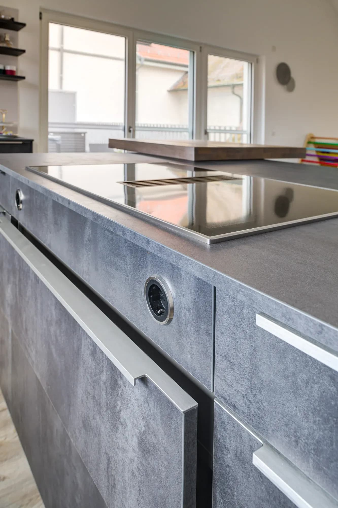 Detail der Kochinsel: Induktionskochfeld mit BORA-Muldenlüftung in der grauen Arbeitsplatte, darunter grifflose Auszüge in Beton-Optik.