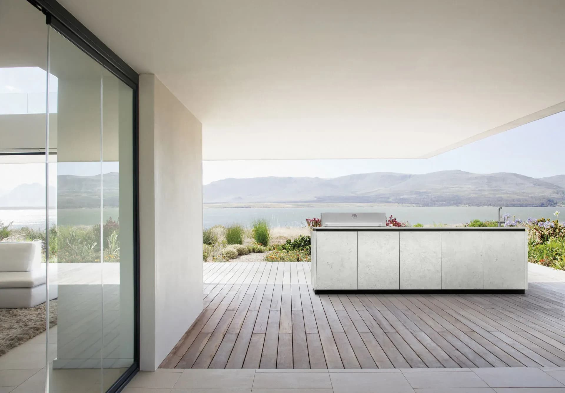 Helle BURN-Outdoor-Küche mit Keramikfronten auf einer überdachten Terrasse mit Blick auf einen See und Hügel