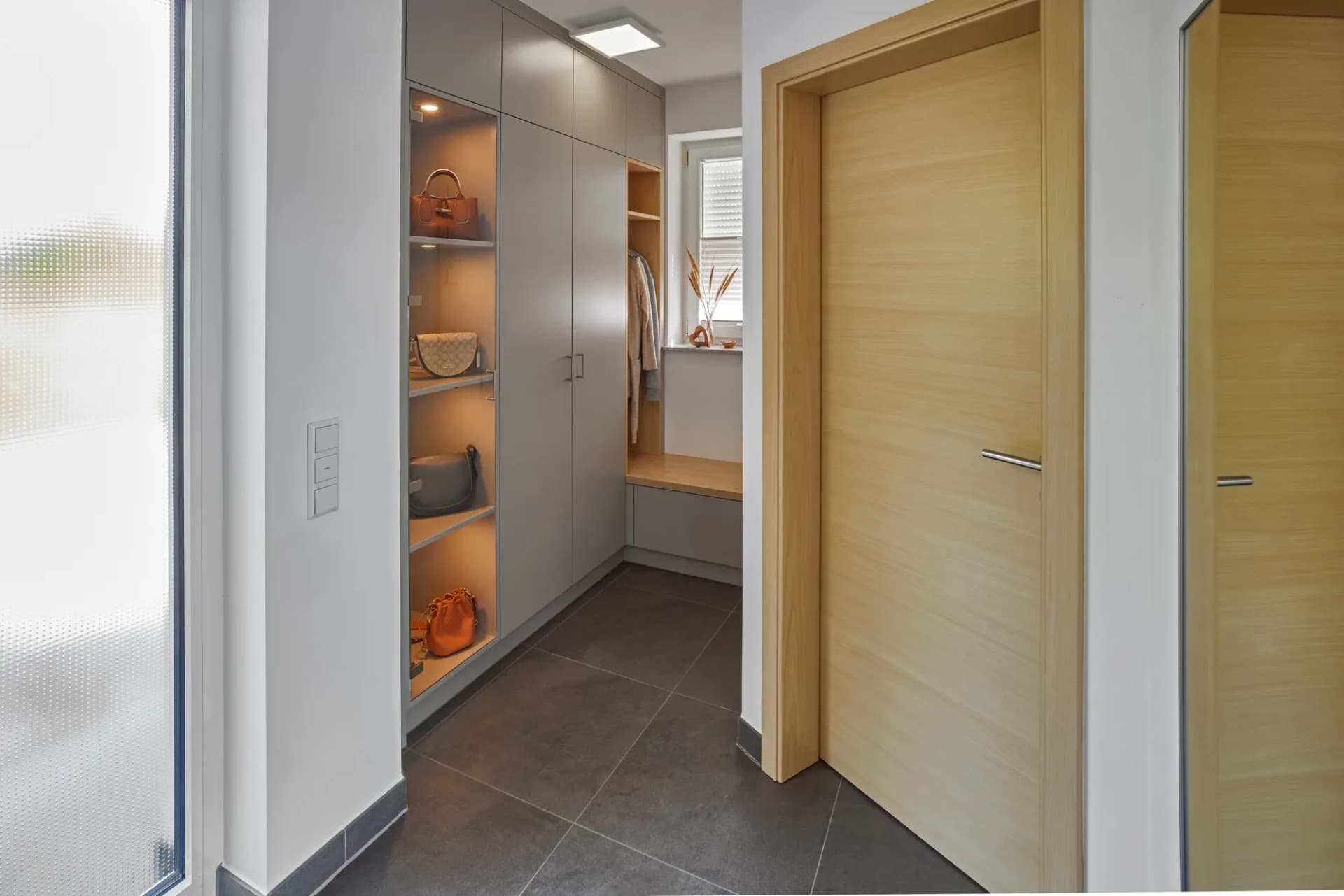 Helle Holz-Zimmertür mit schmalem Griff im Flur, dahinter der lichtgraue Garderobenschrank mit beleuchteter Nische.