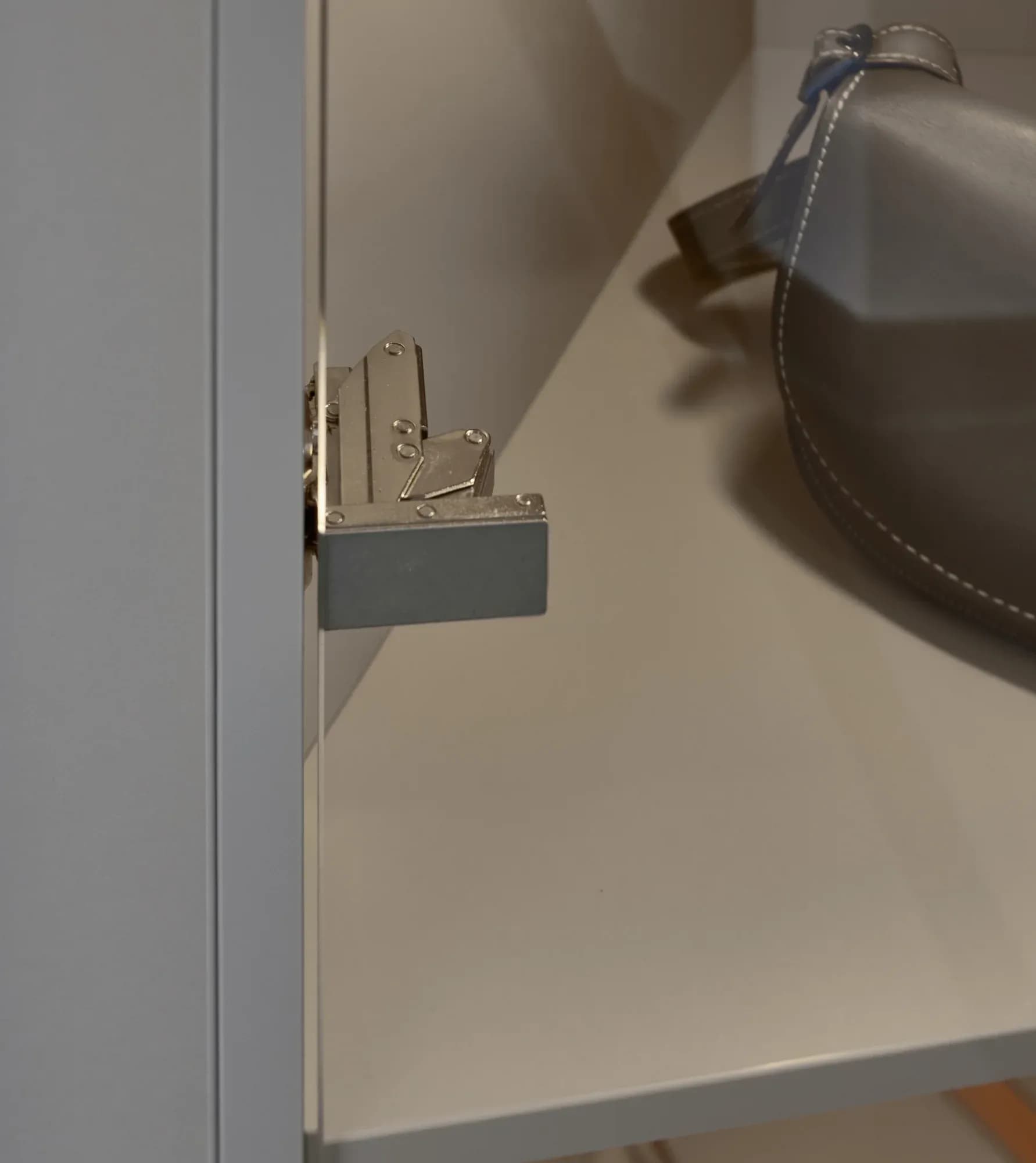 Detail eines Möbelbeschlags: ein gedämpfter Beschlag im Inneren des grauen Schranks über einem Ablageboden.