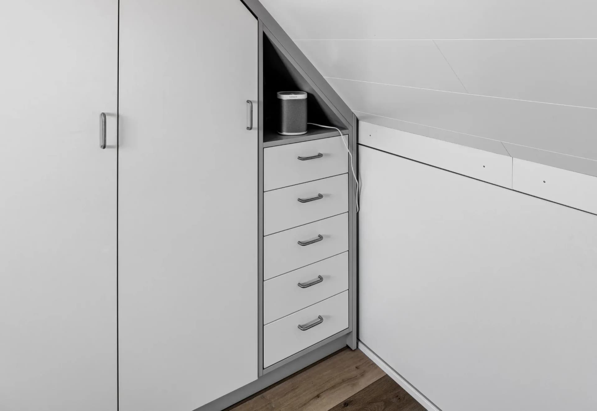 Detail eines Einbauschranks unter der Dachschräge: ein offenes Nischenfach mit Lautsprecher über einem Schubladenturm, rechts flache Schränke am Kniestock.