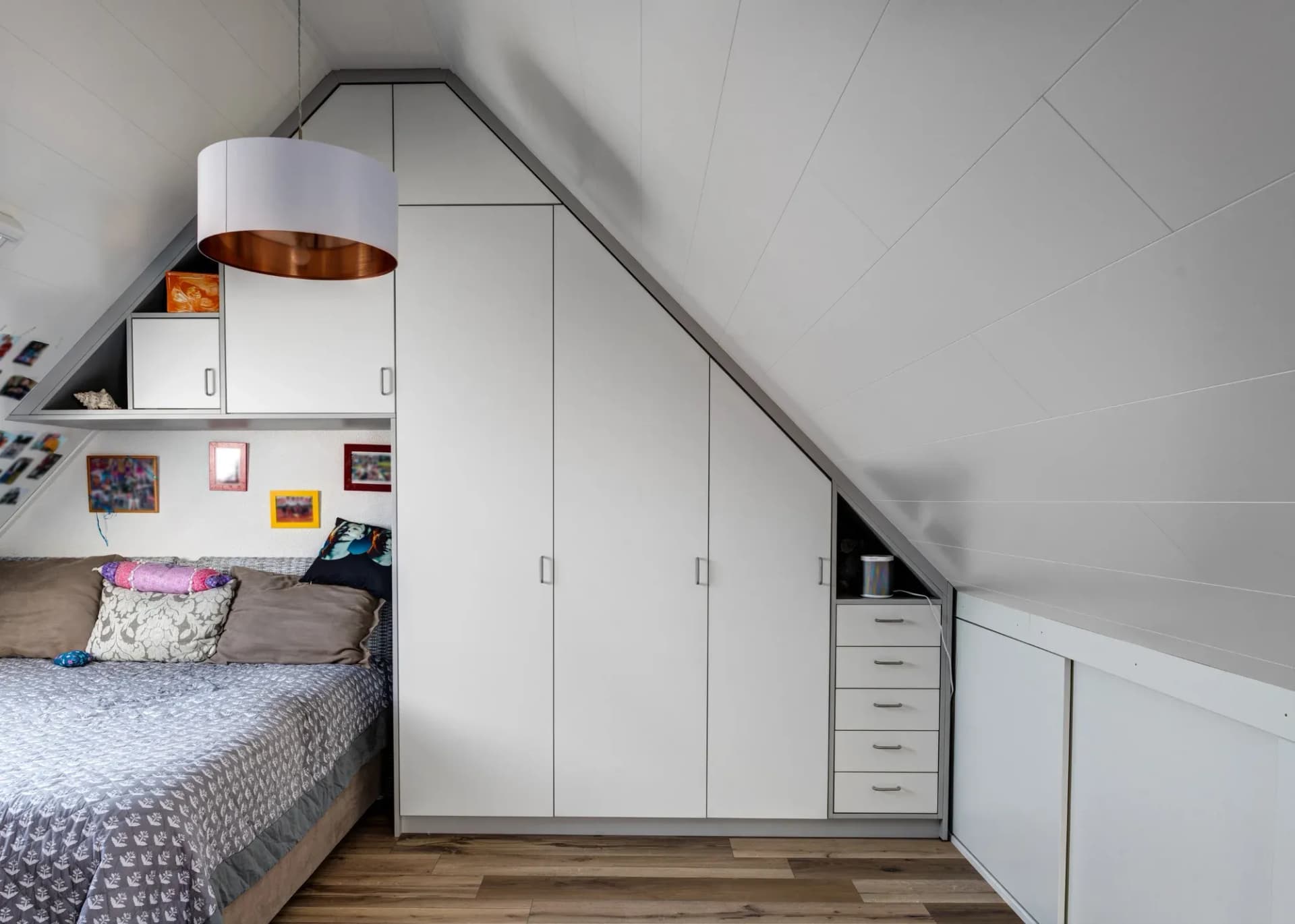 Dachgeschoss-Zimmer mit raumhohem Einbauschrank, der der Giebelschräge folgt: Oberschränke, hohe Türen und ein Schubladenturm bis unter die Traufe.