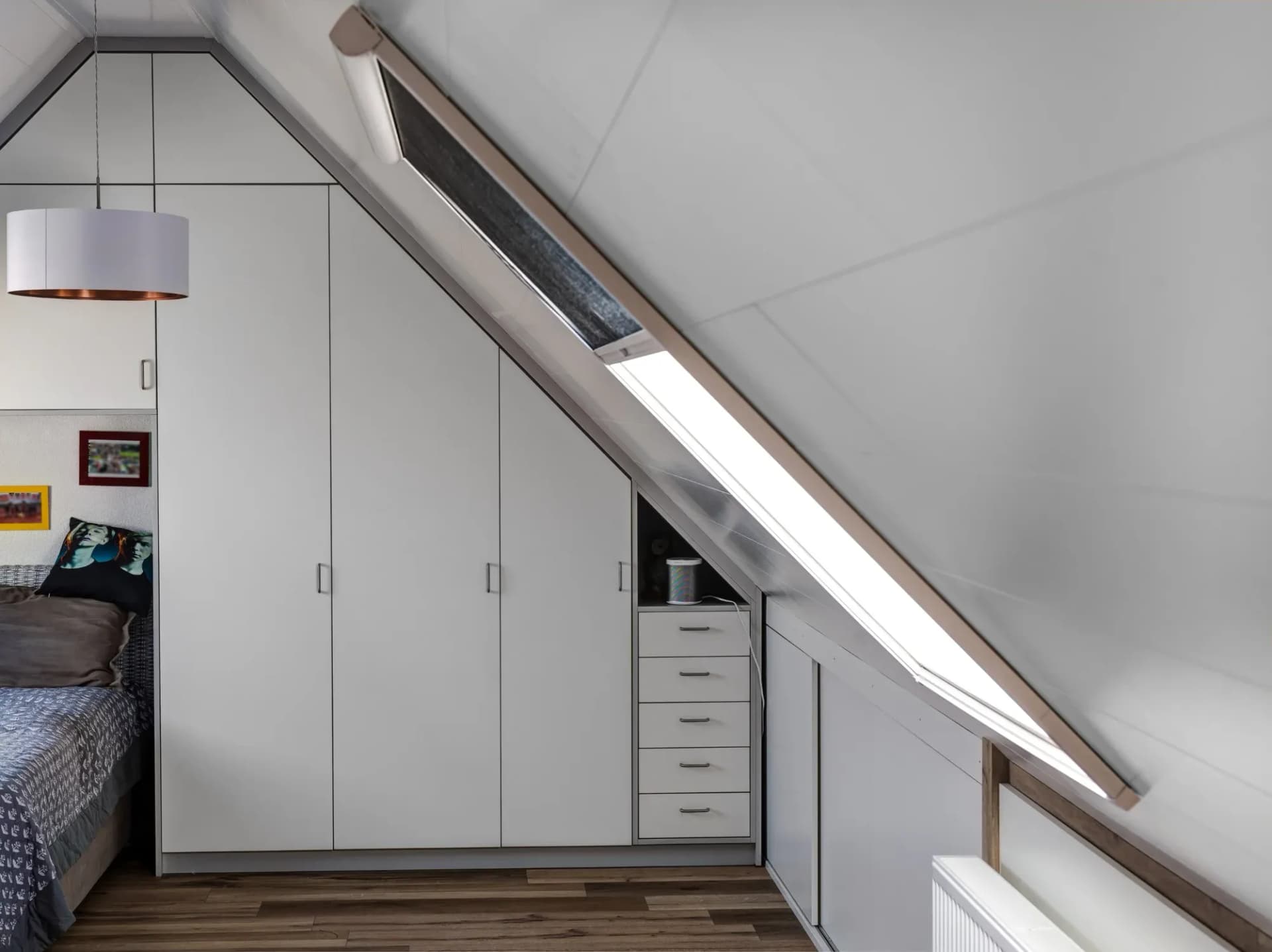Blick entlang der Schrankwand zum Dachfenster: hohe Mattfronten mit Metallgriffen, Tageslicht fällt über die Schräge auf den Schubladenturm.