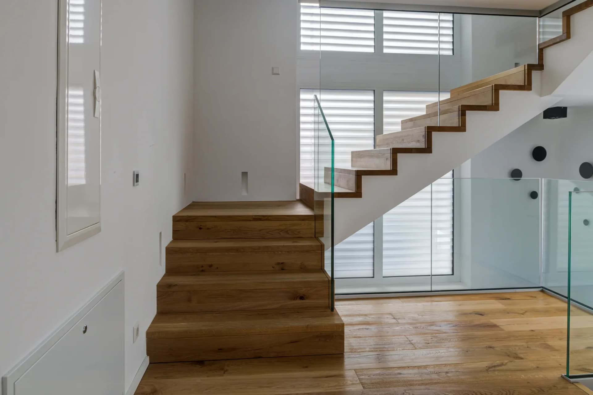 Eichene Faltwerktreppe mit geradem Lauf, gefasst von einem Glasgeländer, im hellen Treppenraum.