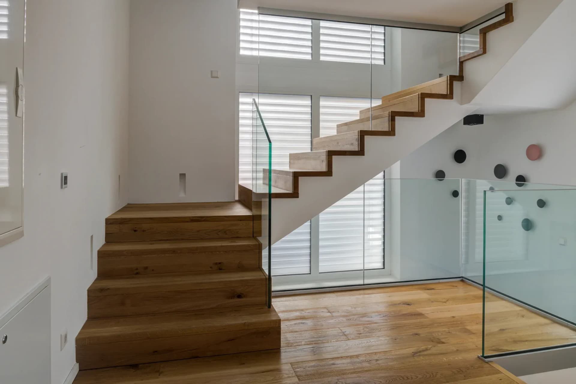 Die Faltwerktreppe in Eiche steigt geradlinig ins Obergeschoss, seitlich ein gläsernes Geländer.