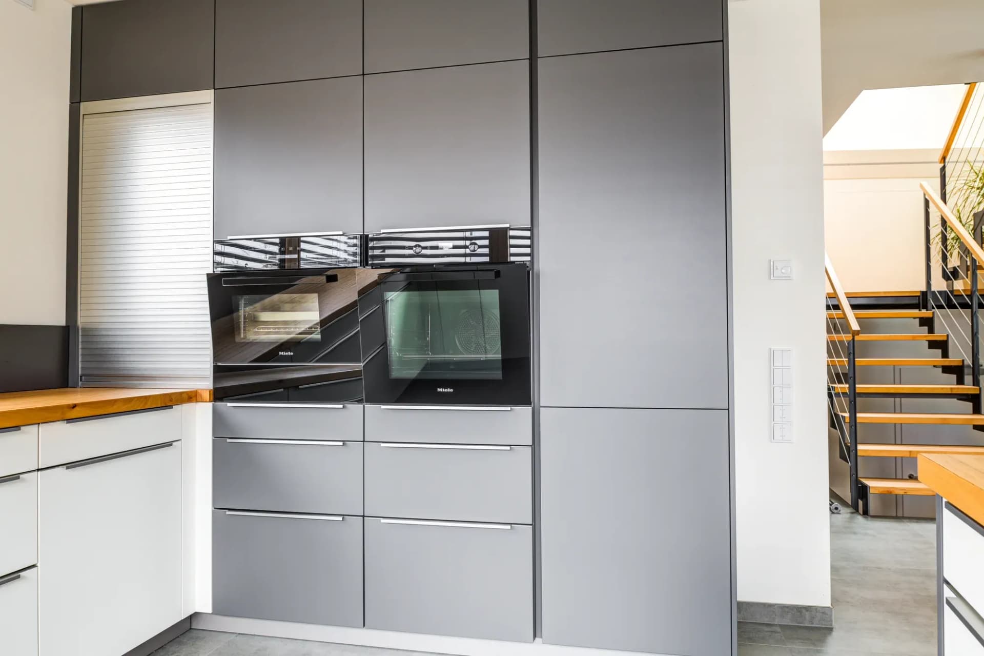 Anthrazitfarbener Hochschrankblock mit eingebautem Miele-Backofen und Kompaktgerät, rechts öffnet sich der Raum zum Treppenhaus.
