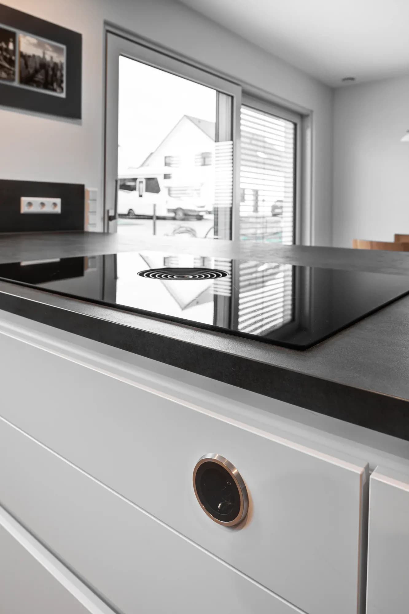 Flächenbündiges schwarzes Induktionskochfeld in der Keramikplatte der weißen Kücheninsel, mit rundem Bedienelement in der Front.
