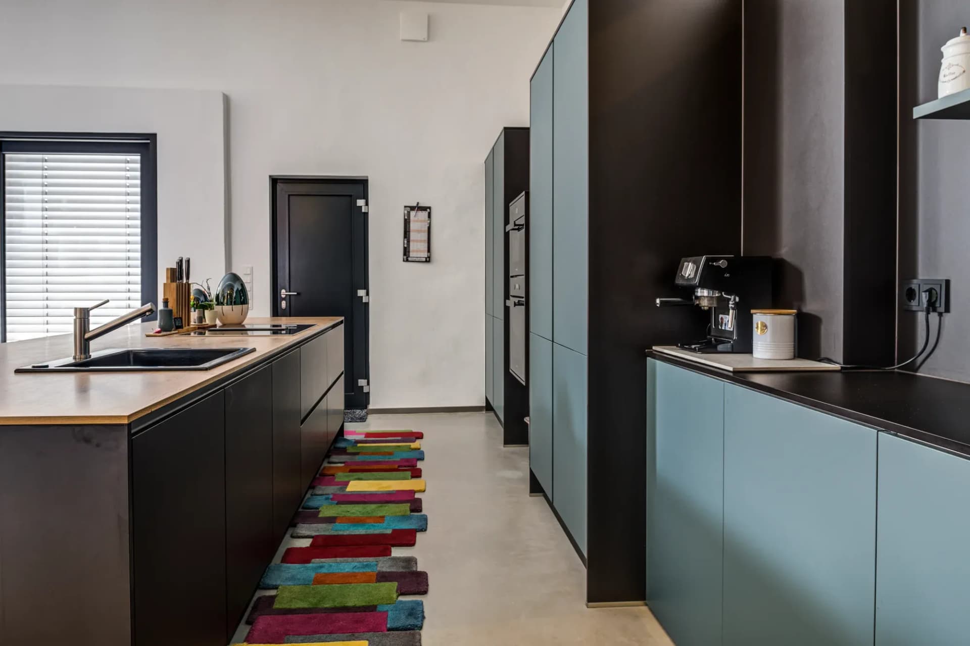 Kücheninsel mit massiver Eiche-Arbeitsplatte und mattschwarzem Korpus, im Hintergrund die Gerätewand.