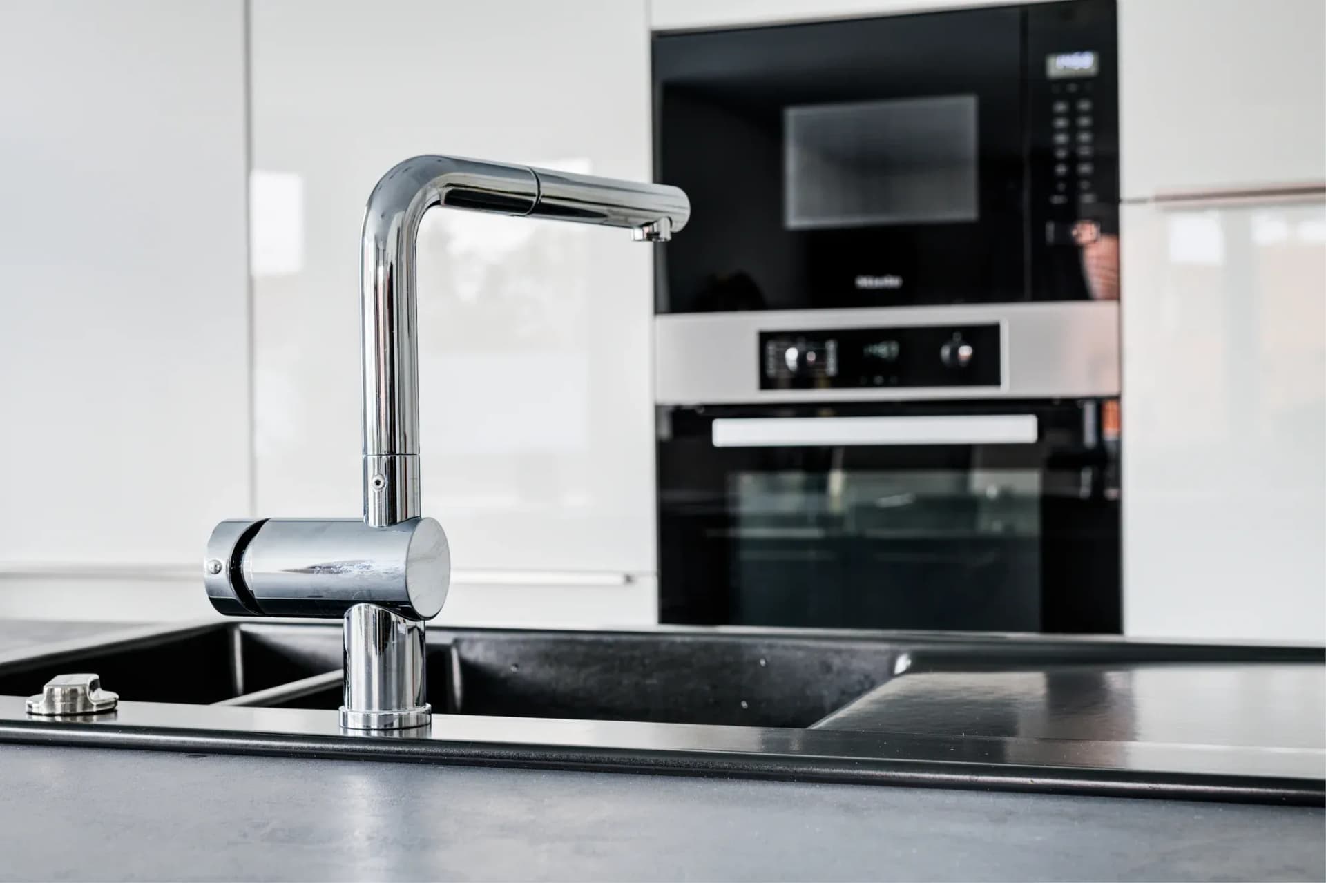 Detail der Küche: hohe Armatur an der Spüle, daneben bündig eingebauter Backofen und Kompaktgerät.