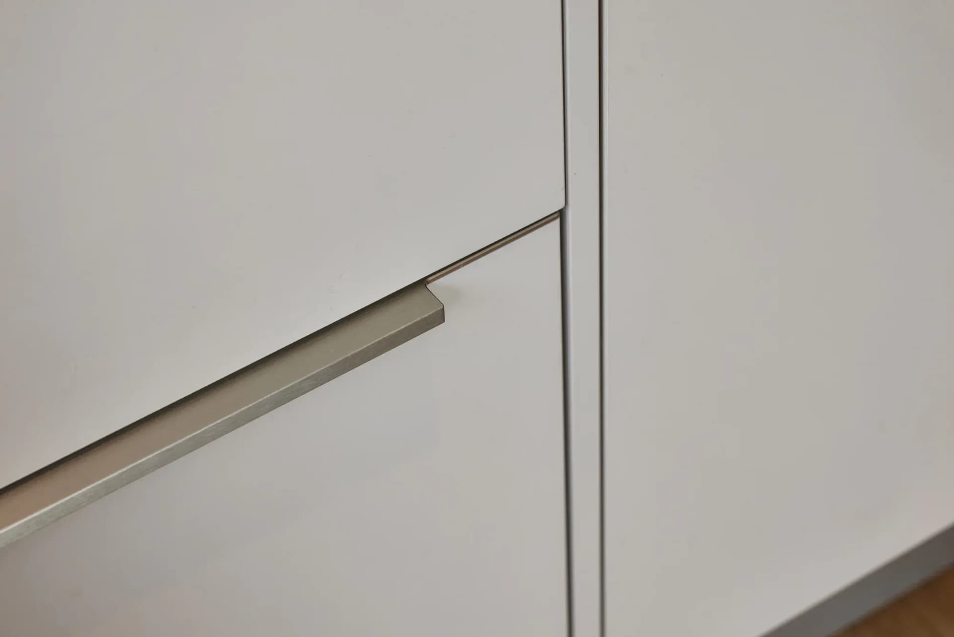 Nahaufnahme der grifflosen Fronten mit schmalem Metallgriff und feiner Kantenfuge in Kaschmirgrau.