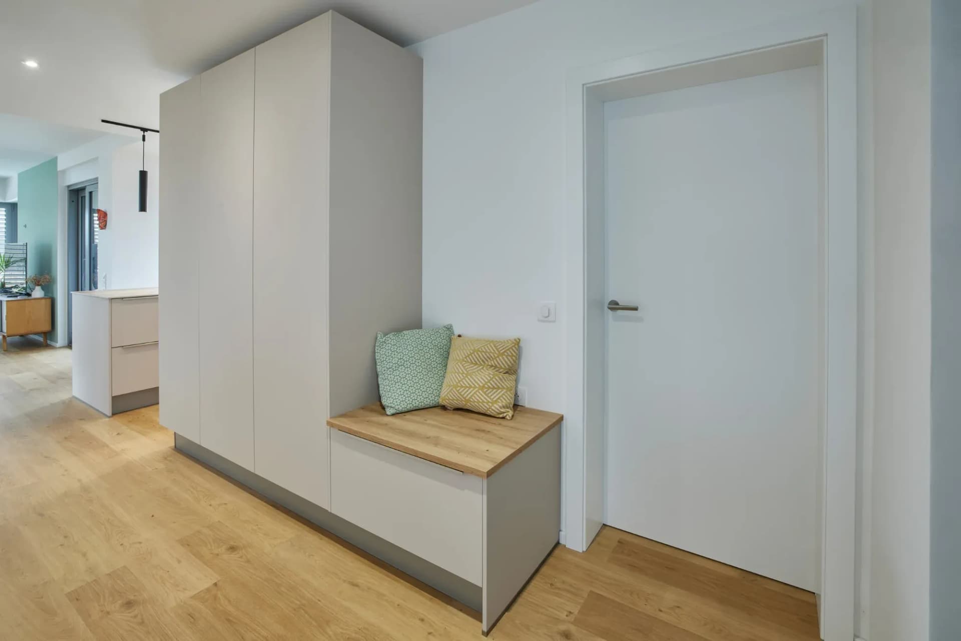 Eingangsbereich mit heller Sitzbank aus Holz vor der Garderobenwand, zwei Kissen und Blick in den Flur.