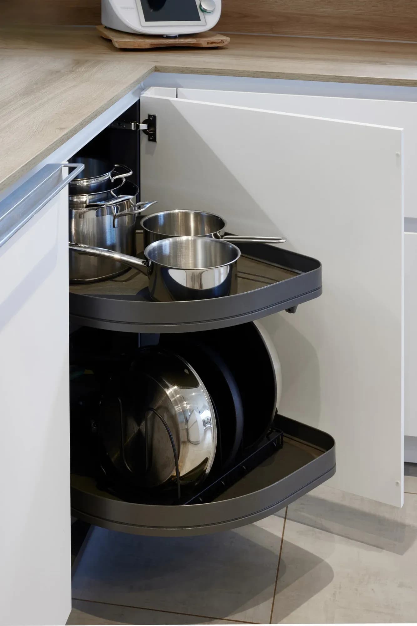 Geöffneter Eckschrank mit Karussellauszug, beladen mit Edelstahltöpfen und Pfannen.