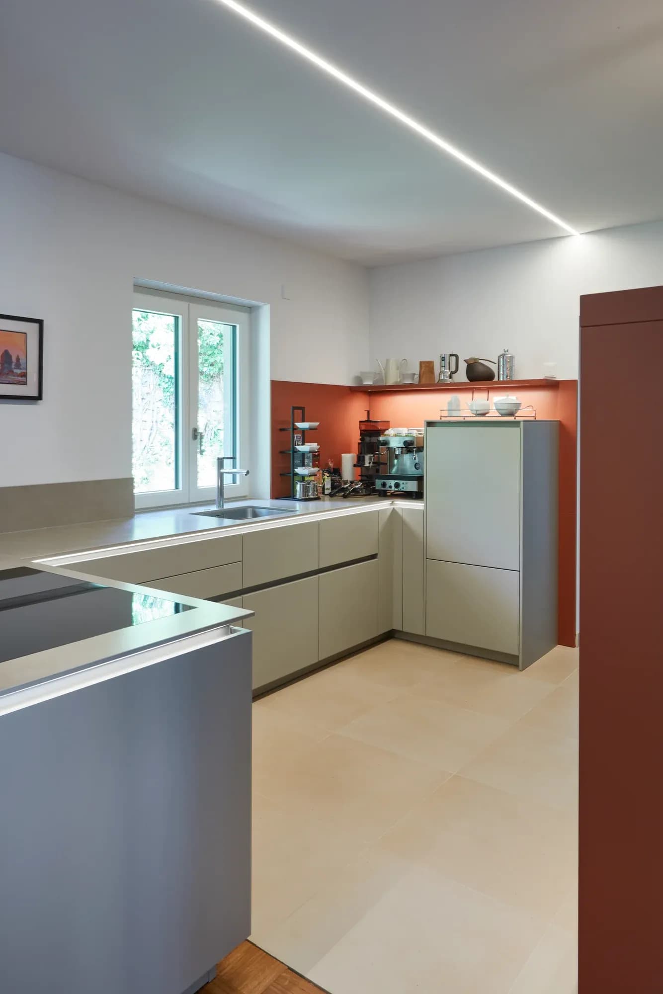 Spülzeile am Fenster mit grauer Arbeitsfläche vor einer terrakottafarbenen Wand, seitlich graubeige Hochschränke.