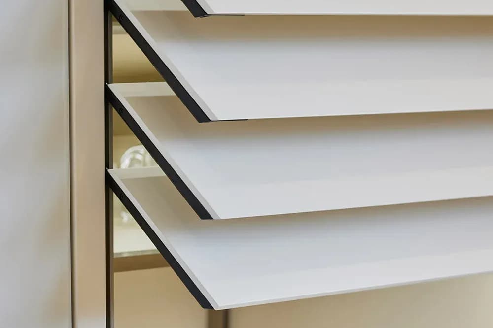 Detail des integrierten Hochschranks: halb geöffneter elektrischer Rollladen mit weißen Lamellen gibt den Blick in den beleuchteten Schrank frei.