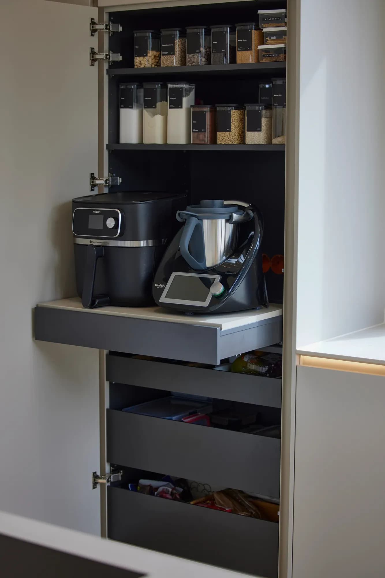 Geöffneter Hochschrank-Auszug mit Vorratsgläsern, Küchenmaschine und Kaffeevollautomat.