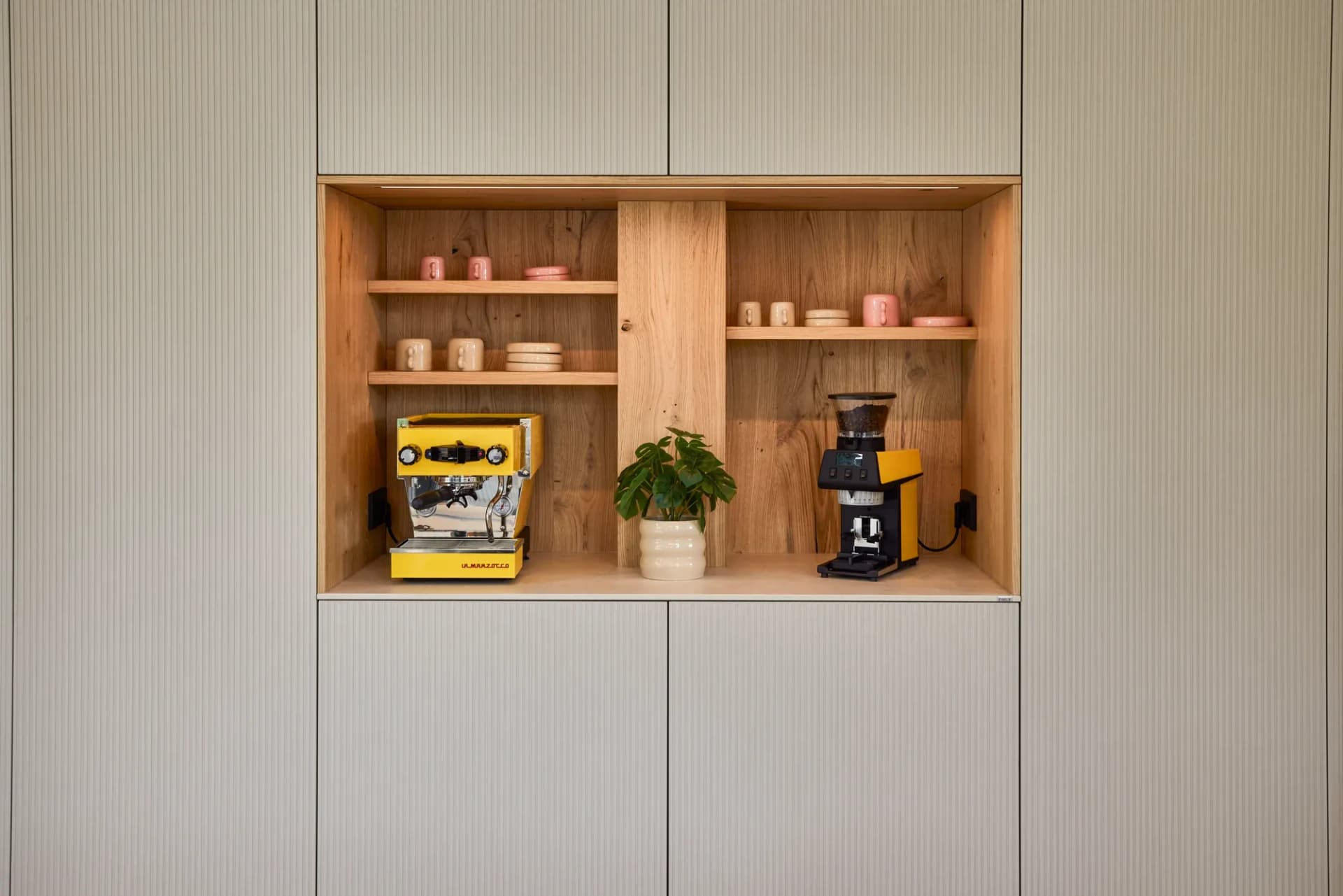 Offene Eichennische mit gelber Siebträger-Espressomaschine, Mühle, Tassen und Pflanze.