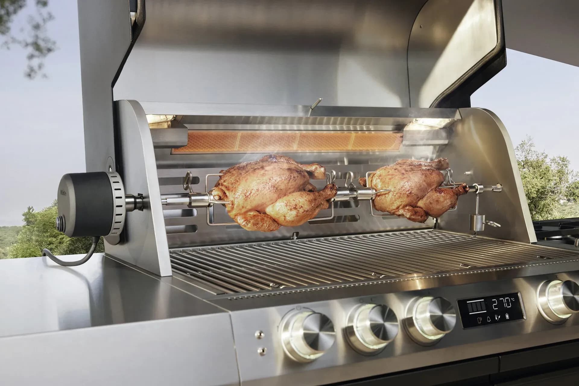 Zwei Hähnchen drehen sich am Rotisserie-Spieß in einem geöffneten Miele-Grill, das Display zeigt 270 Grad