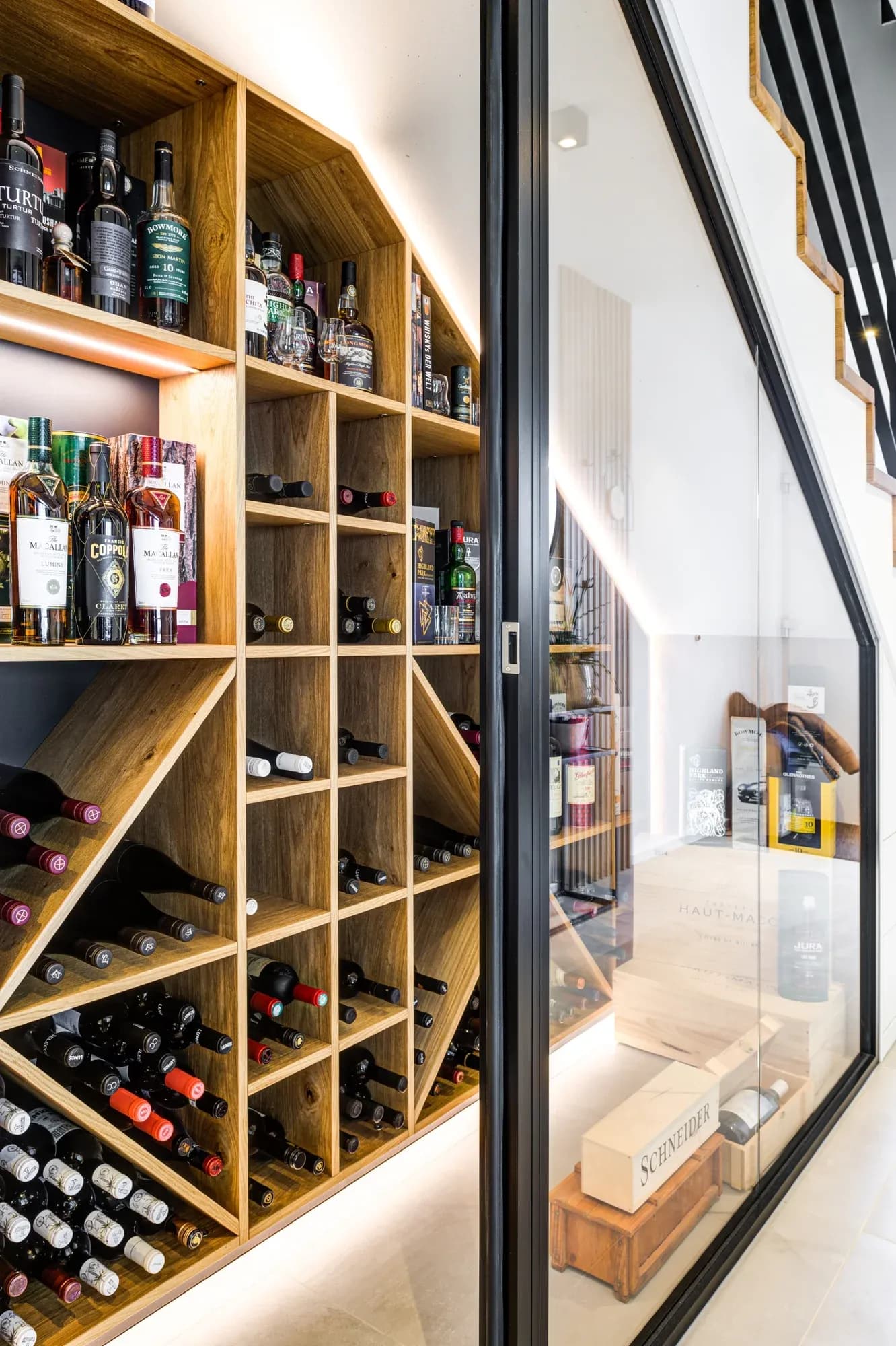Blick auf den verglasten Weinkeller unter der Treppe: links das offene Eichenregal, rechts die schwarze Stahl-Glas-Wand mit indirekter Beleuchtung.