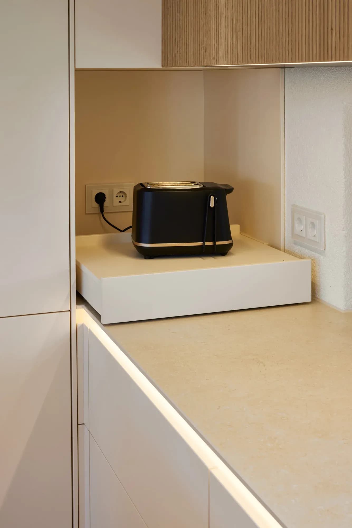 Ausgezogener Geräteauszug in der Hochschrankwand mit Toaster an eigener Steckdose, daneben die helle Keramik-Arbeitsplatte mit indirekter Beleuchtung.