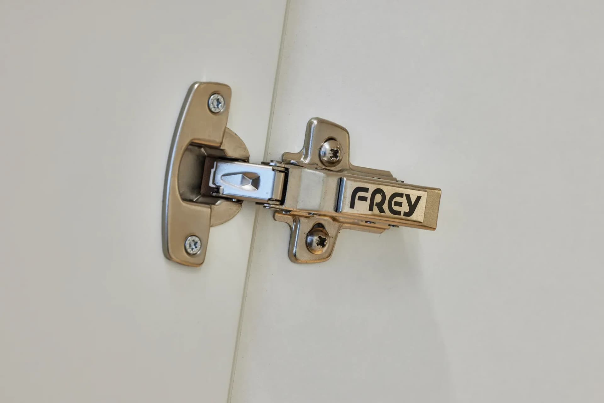 Detail eines Möbelscharniers mit der Gravur FREY an einer weißen Schrankfront.