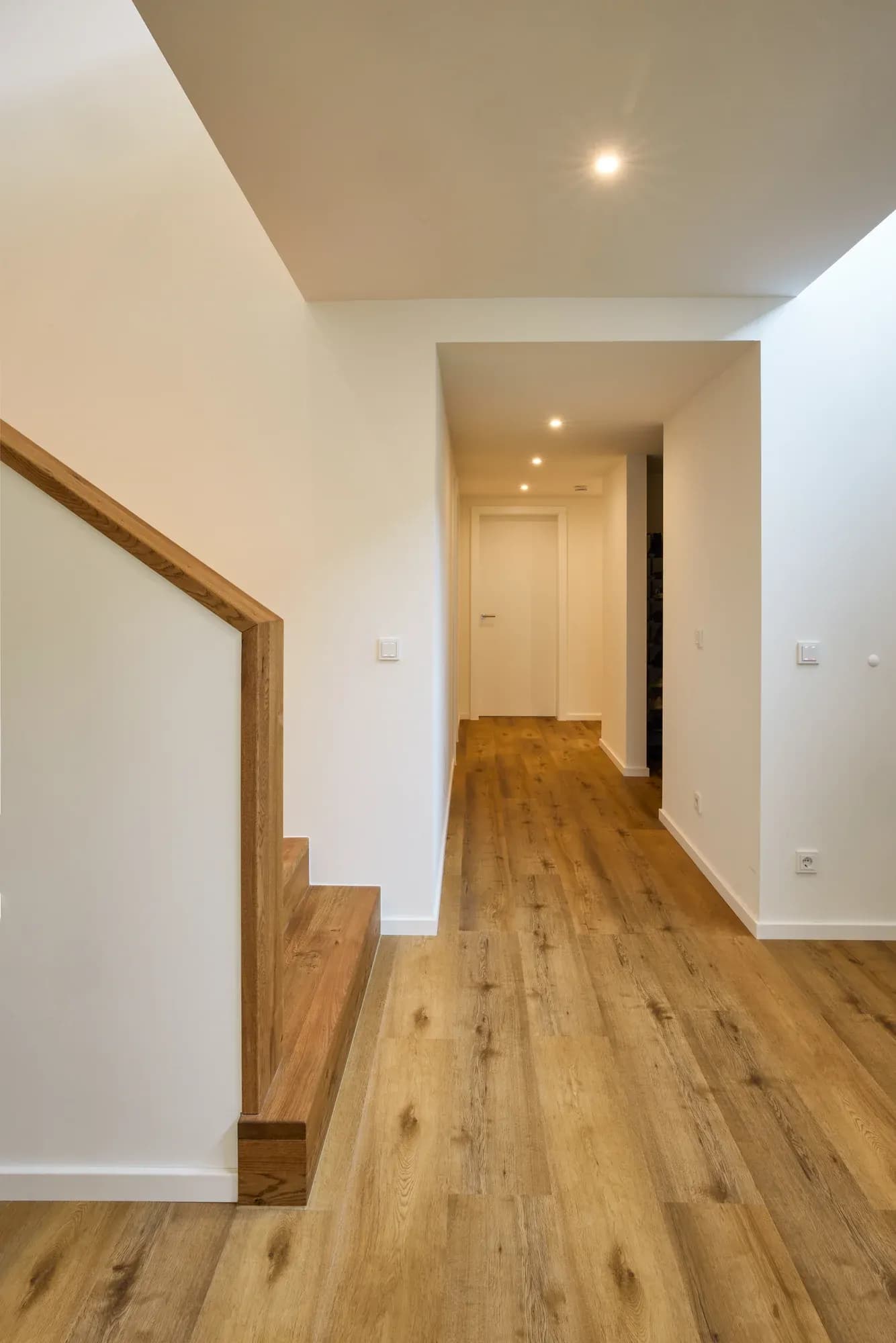 Faltwerk-Treppe aus massiver Eiche mit indirekt beleuchtetem Handlauf vor einer weißen Wand.