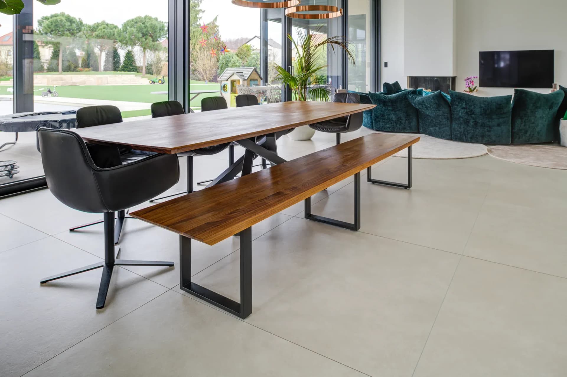 Ess- und Wohnbereich mit Holztafel, Sitzbank, raumhoher Verglasung und grünem Sofa