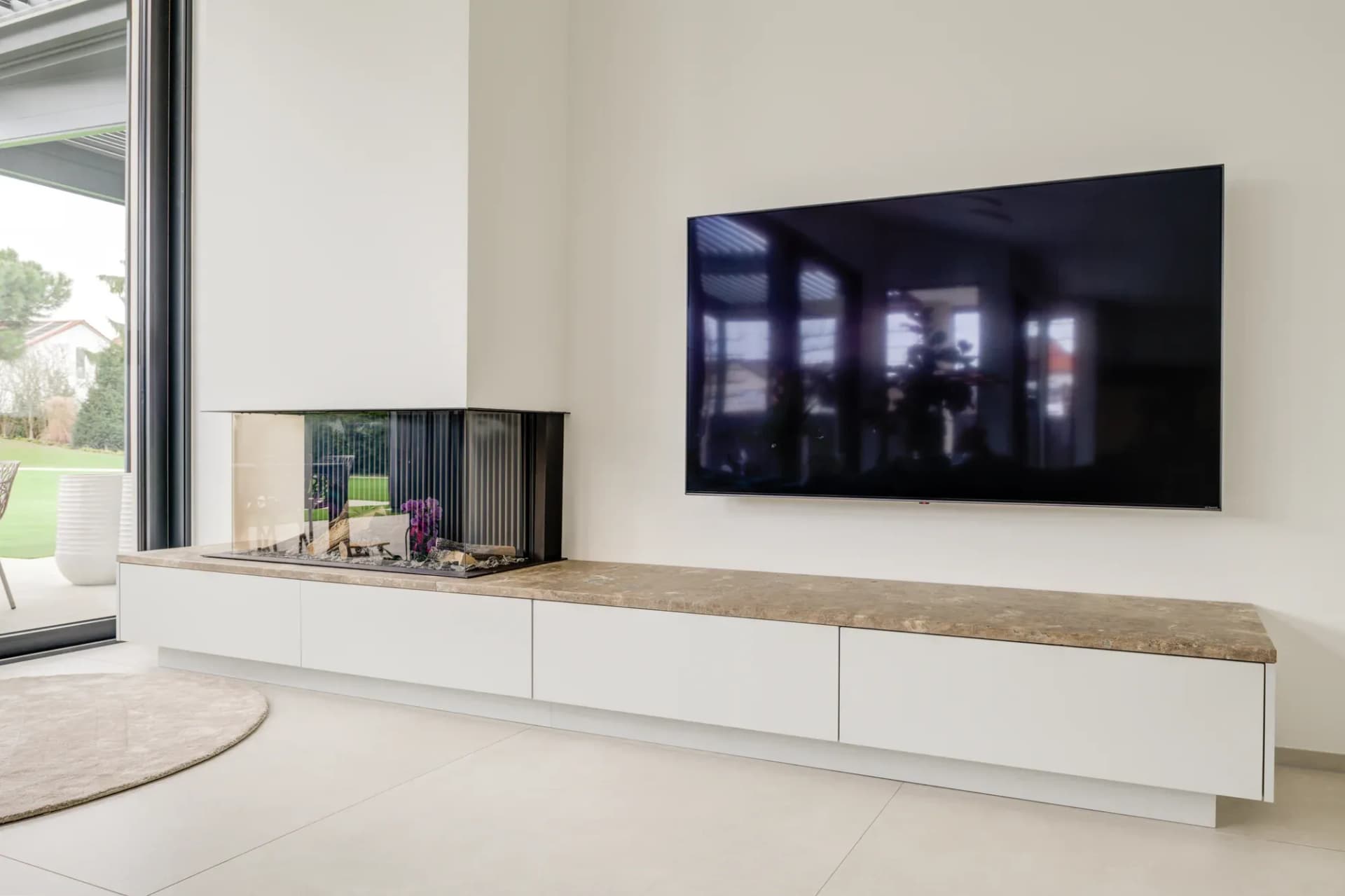 Wohnbereich mit Eckkamin, wandhängendem Sideboard mit Steinplatte und großem Fernseher