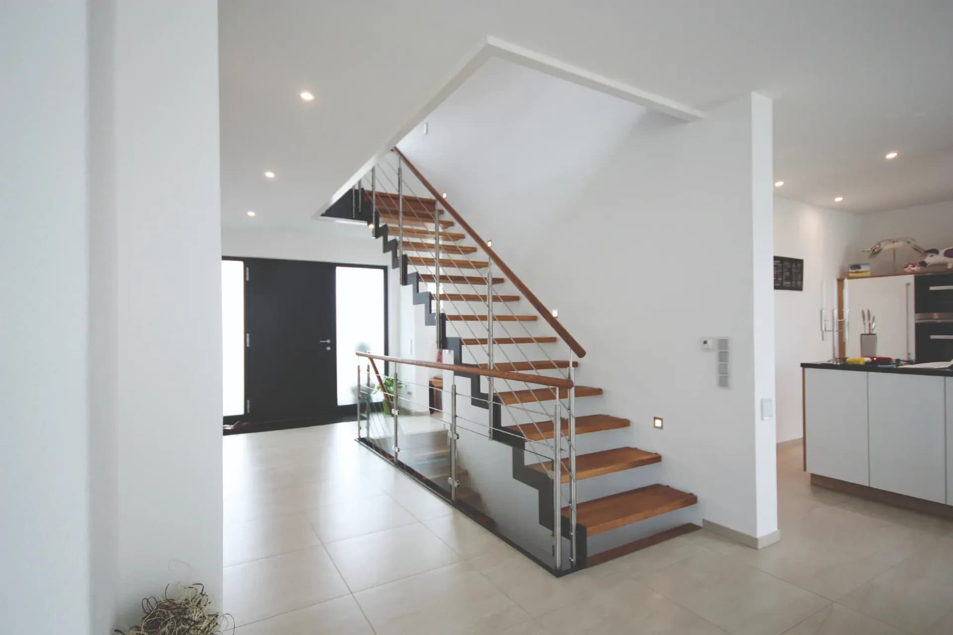 Treppe mit gezackter Stahlwange, Holzstufen und Edelstahlgeländer zwischen Flur und offener Küche