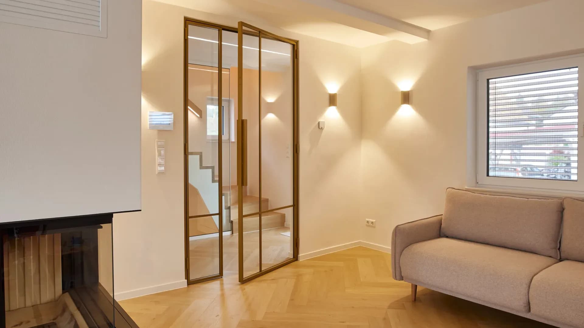 Zweiflügelige Glastür im Loft-Stil mit bronzefarbenem Sprossenrahmen zum Treppenhaus, davor Fischgrätparkett und ein Sofa