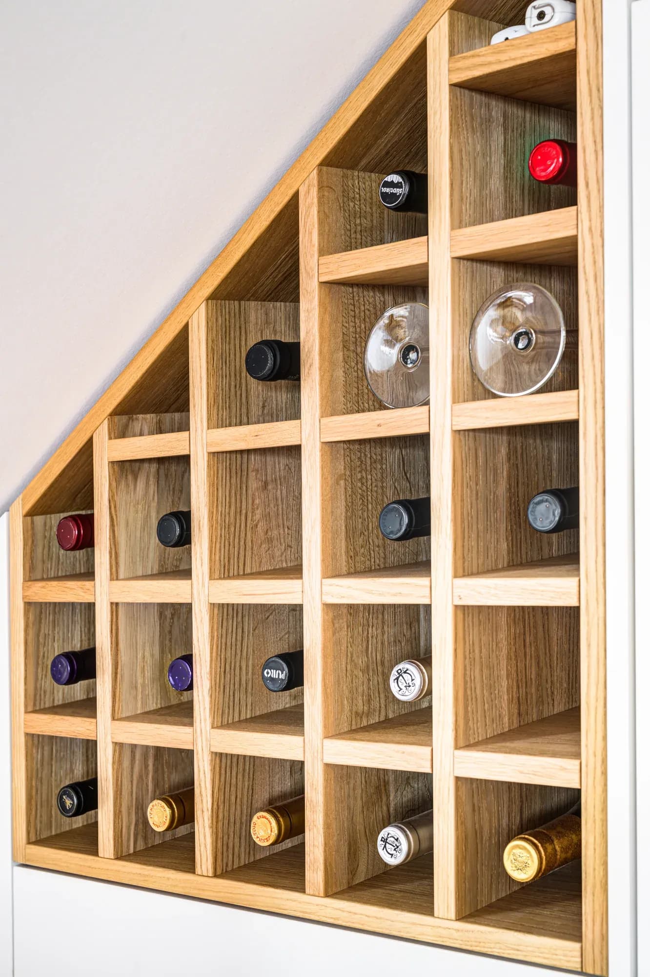 Detail des maßgefertigten Weinregals aus Eiche mit einzelnen Fächern für Flaschen und Gläser, exakt in den Winkel des Daches gesetzt.
