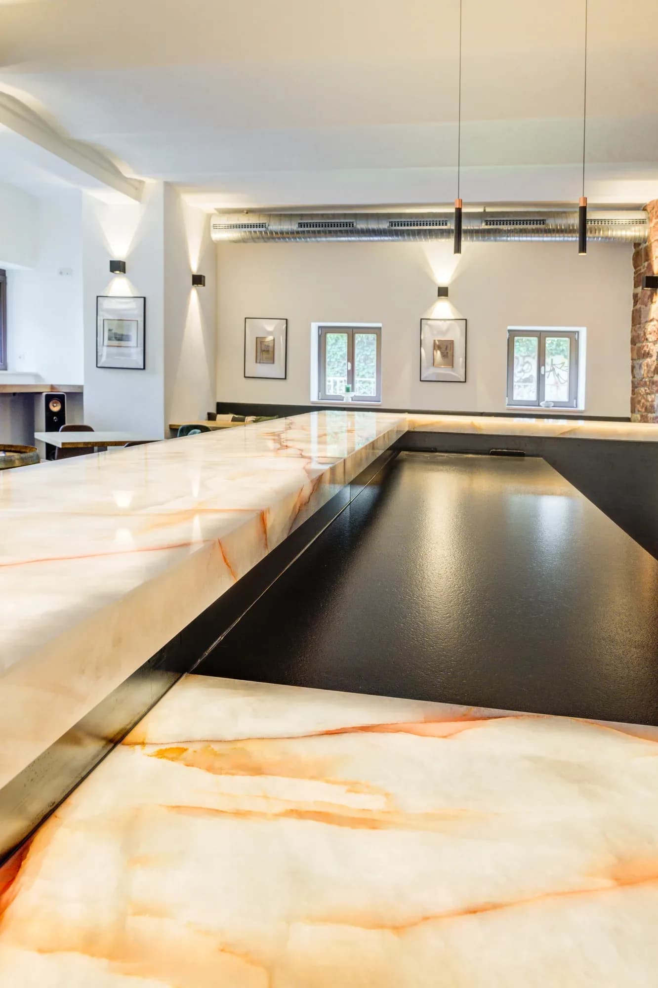 Hinterleuchtete Onyx-Theke mit angesetzter schwarzer Arbeitsfläche in einem hohen Raum mit gerahmten Bildern und Fenstern.
