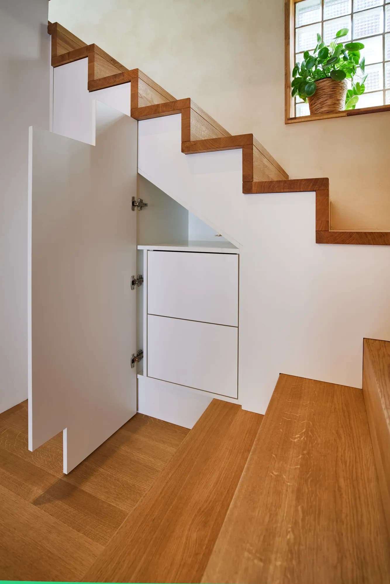 Geöffnete Schranktür unter der Treppe: im Inneren ein eingebauter weißer Schuhschrank mit Klappfächern.