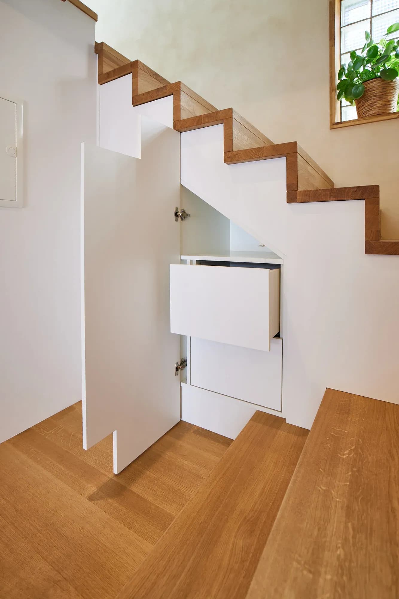 Der Stauraum unter der Treppe in Benutzung: ein weißer Auszug ist nach vorn herausgezogen.