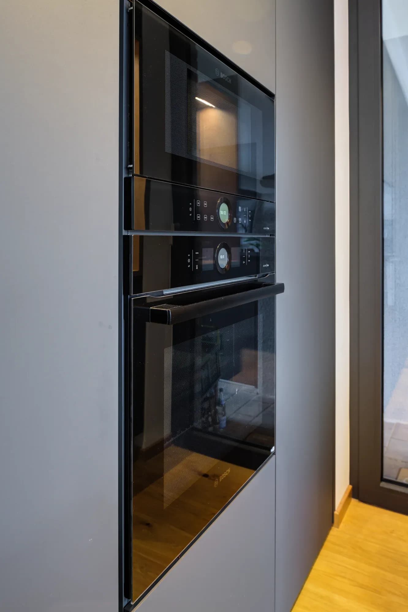 Anthrazitfarbener Hochschrank mit Gerät hinter schwarzem Glas.