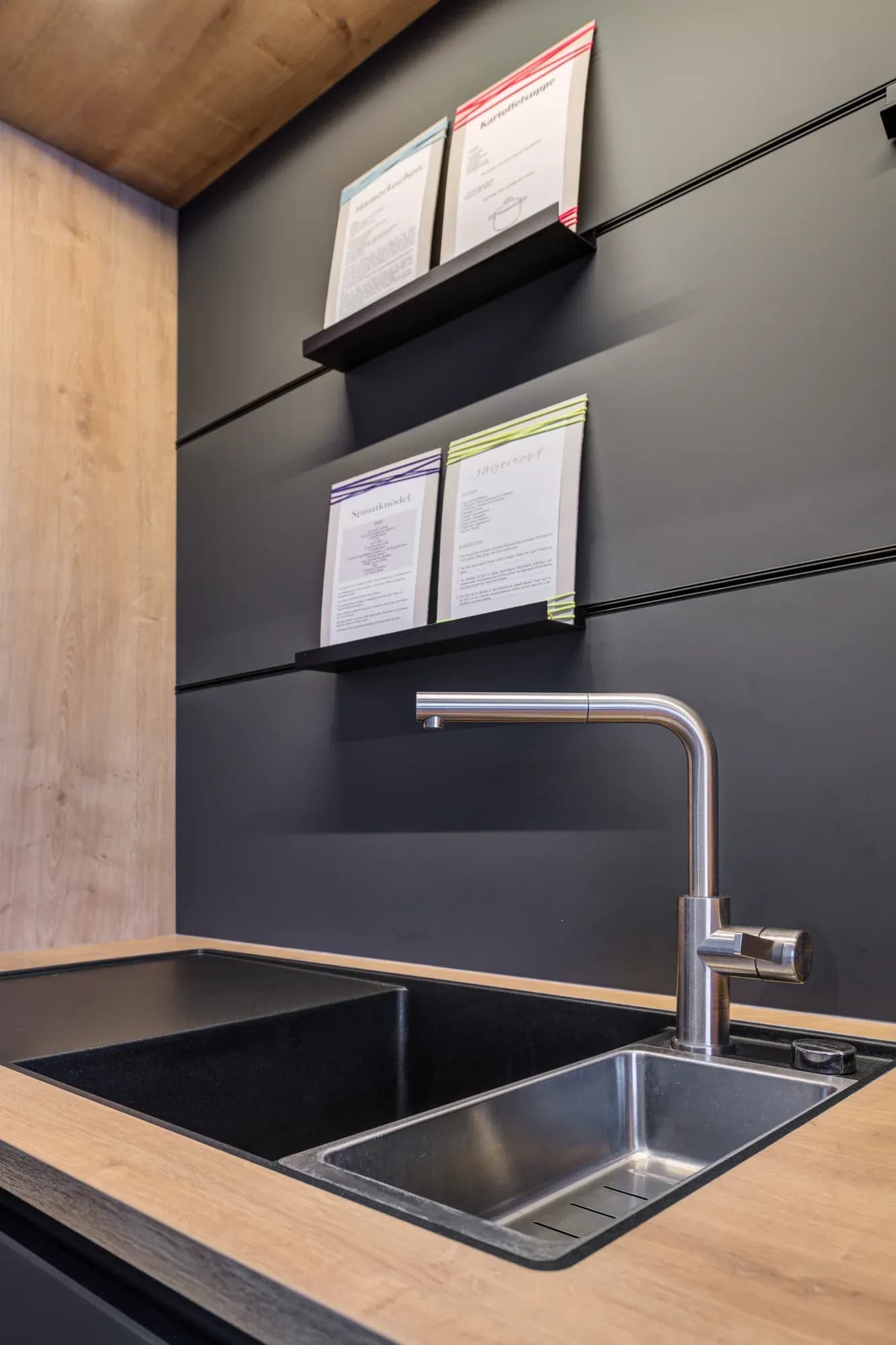 Hauswirtschaftsbereich mit Massivholz-Arbeitsplatte, Edelstahlspüle und schwarzer Paneelwand.