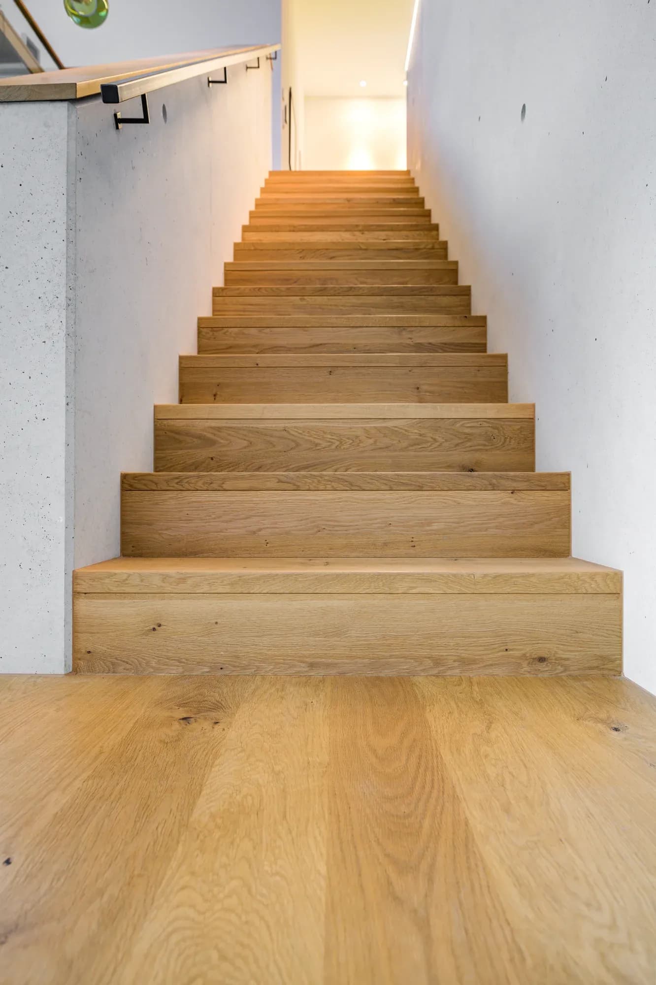 Blick eine Eichentreppe hinauf ins beleuchtete Obergeschoss.