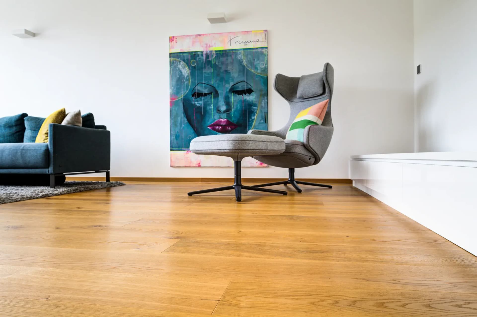 Wohnraum mit Eichen-Landhausdiele, Sofa, Sessel und Kunstwerk an der Wand.