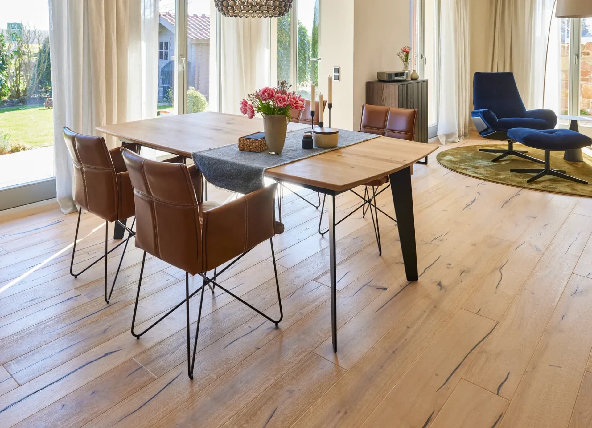 Essbereich mit Eichentisch, cognacfarbenen Lederstühlen und Rattan-Pendelleuchte vor bodentiefen Fenstern zum Garten.