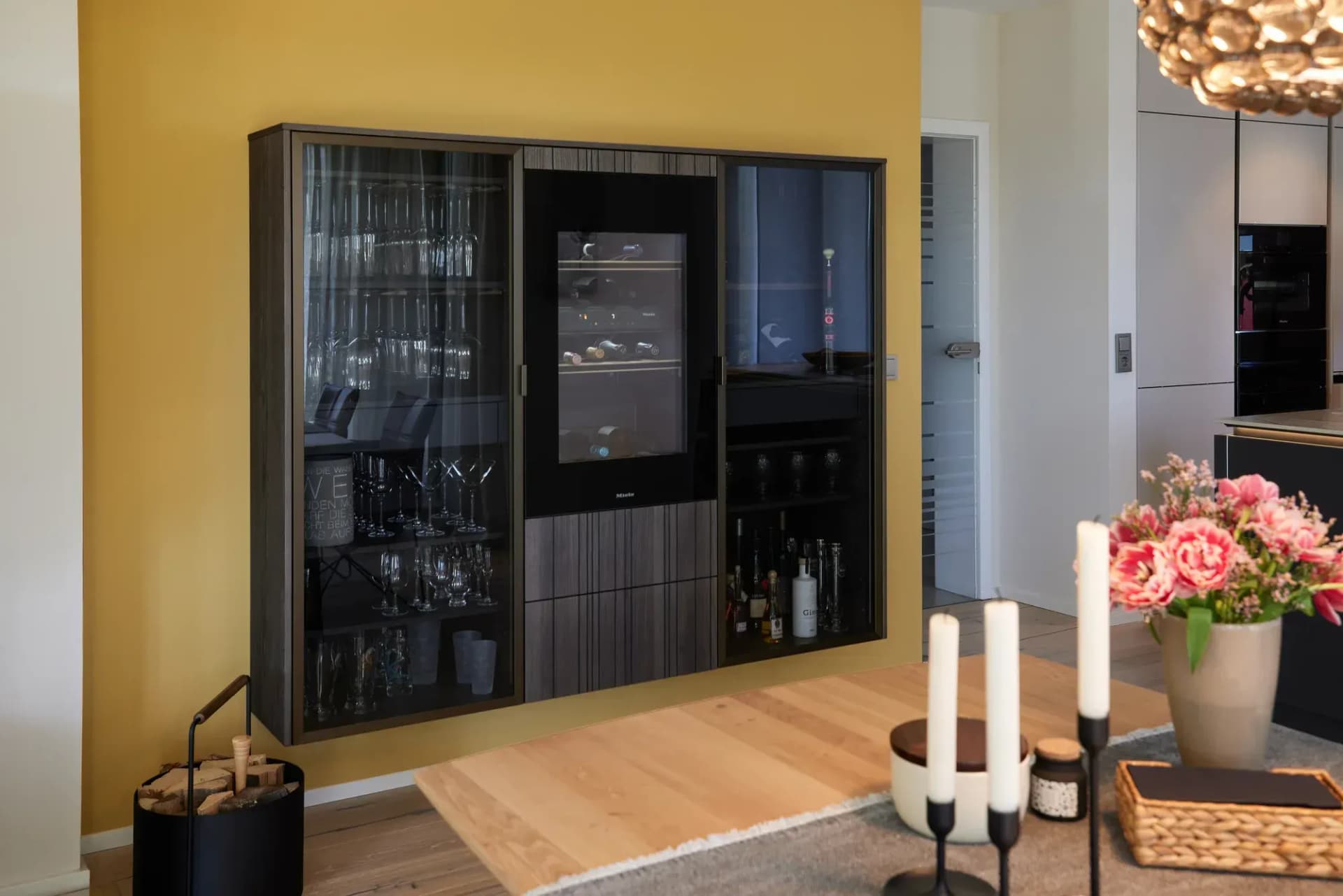 Dunkler Barschrank aus geriffeltem Holz mit integriertem Miele-Weinklimaschrank und Gläservitrine vor senfgelber Wand.