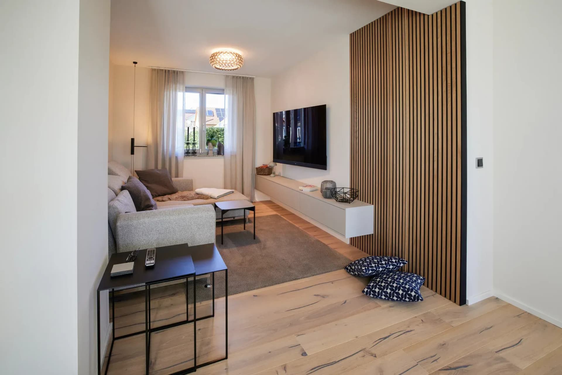 Wohnzimmer mit Eichen-Lamellenwand, schwebendem Lowboard und Wandfernseher über der Eiche-Landhausdiele.