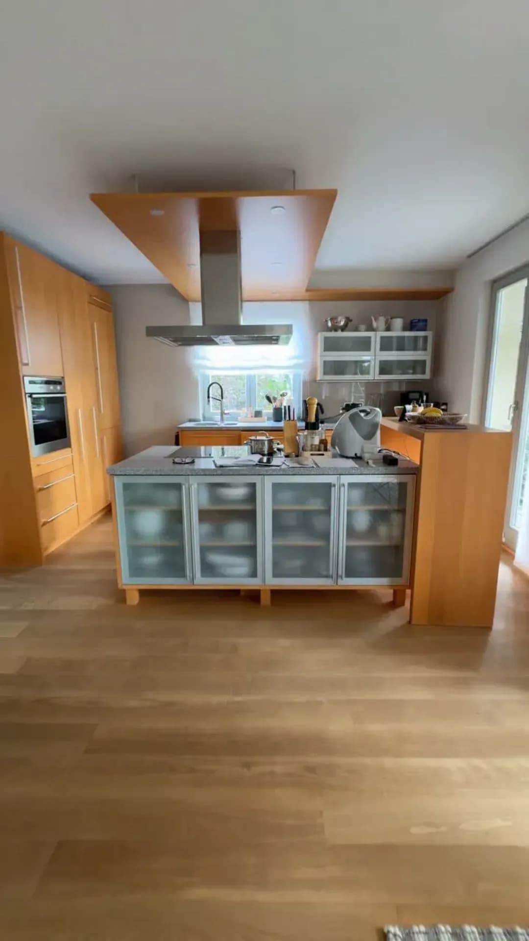 Vorher: die bestehende Küche aus hellem Holz mit freistehender Kochinsel, aufgenommen vor dem Umbau.