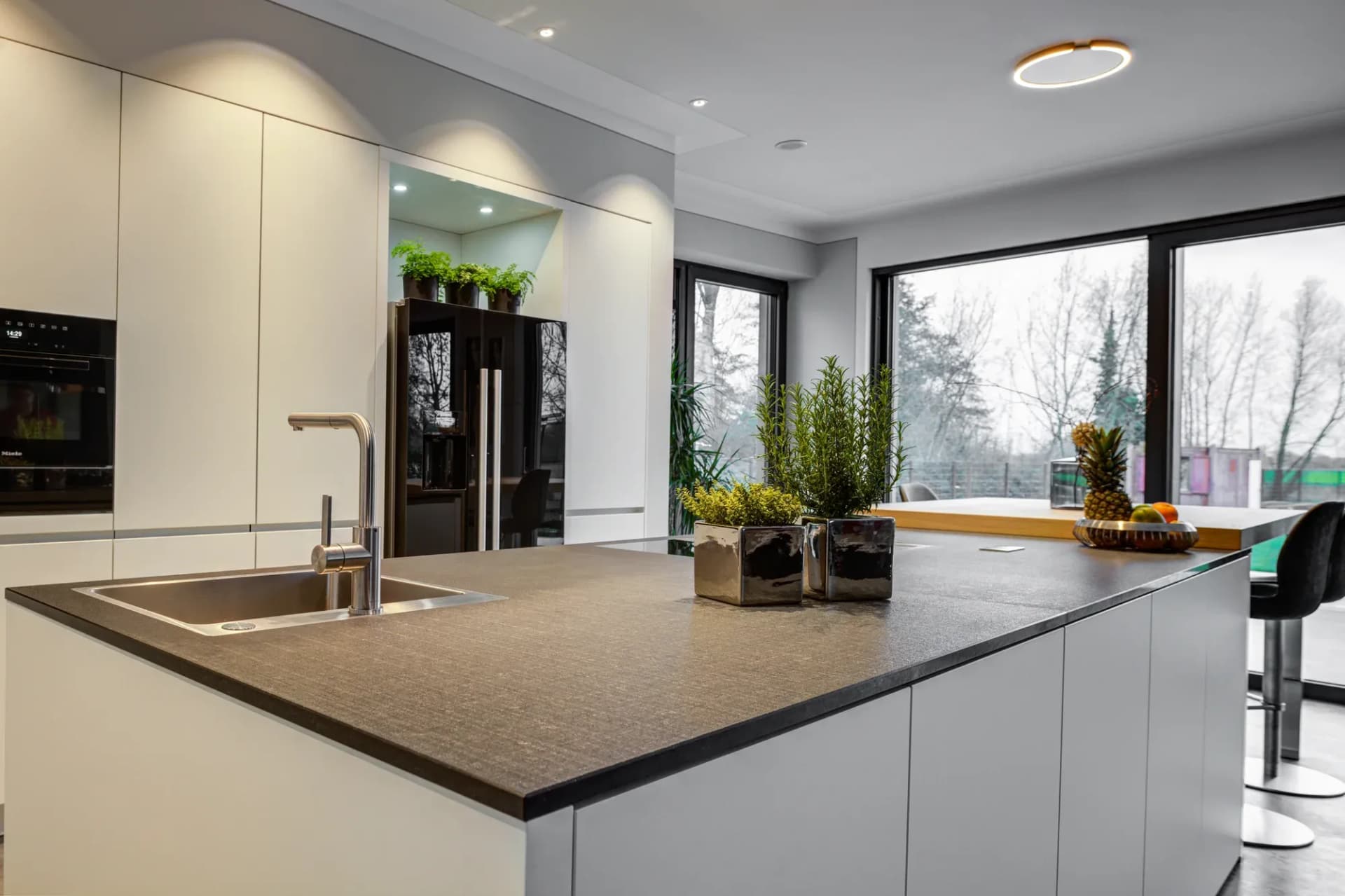 Dunkle Natursteinarbeitsplatte mit unterbautem Edelstahlspülbecken und Blick durch die Fensterfront in den Garten