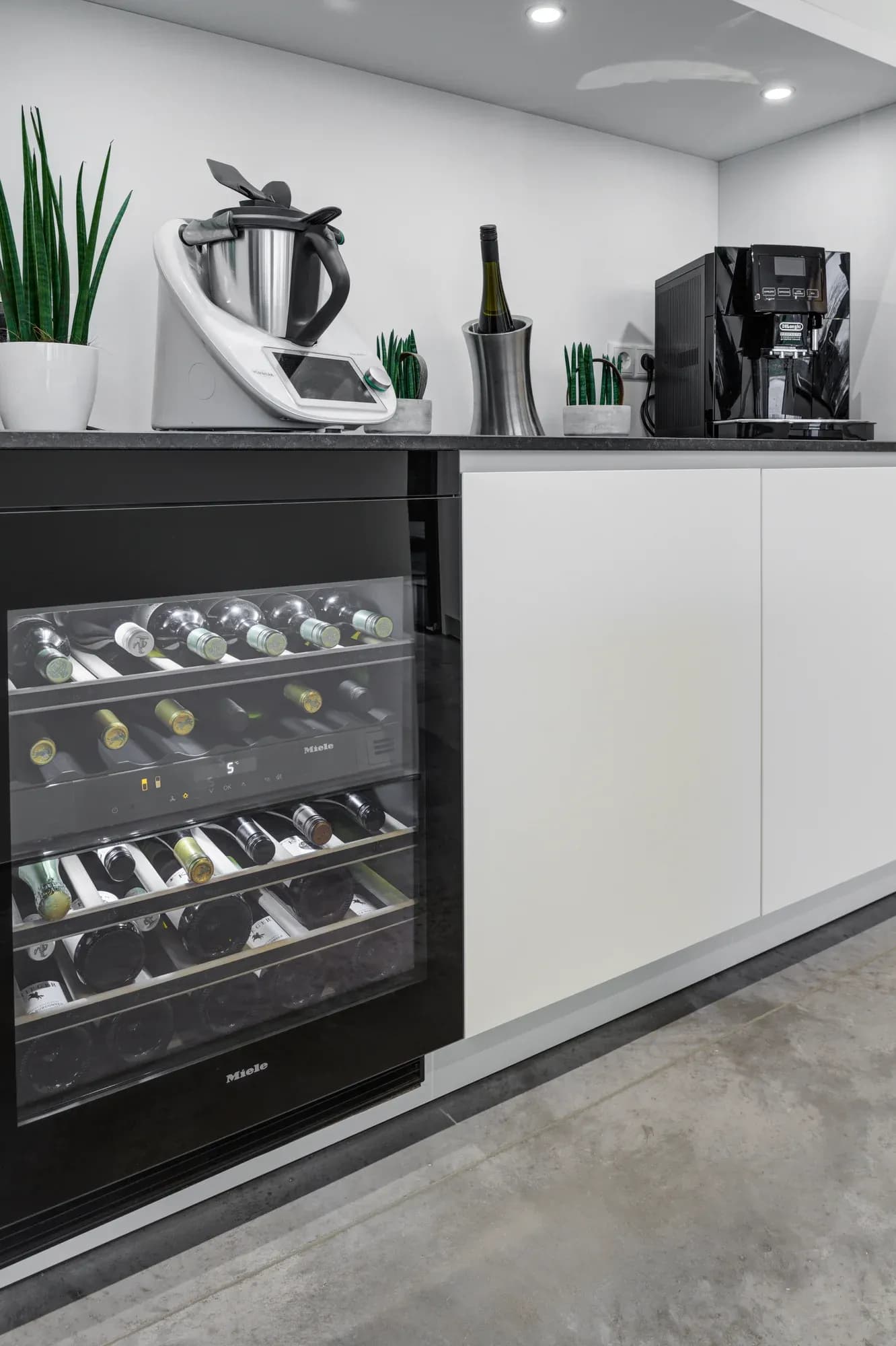 Barzeile mit Miele-Weinklimaschrank, Thermomix und Kaffeevollautomat auf dunkler Steinablage