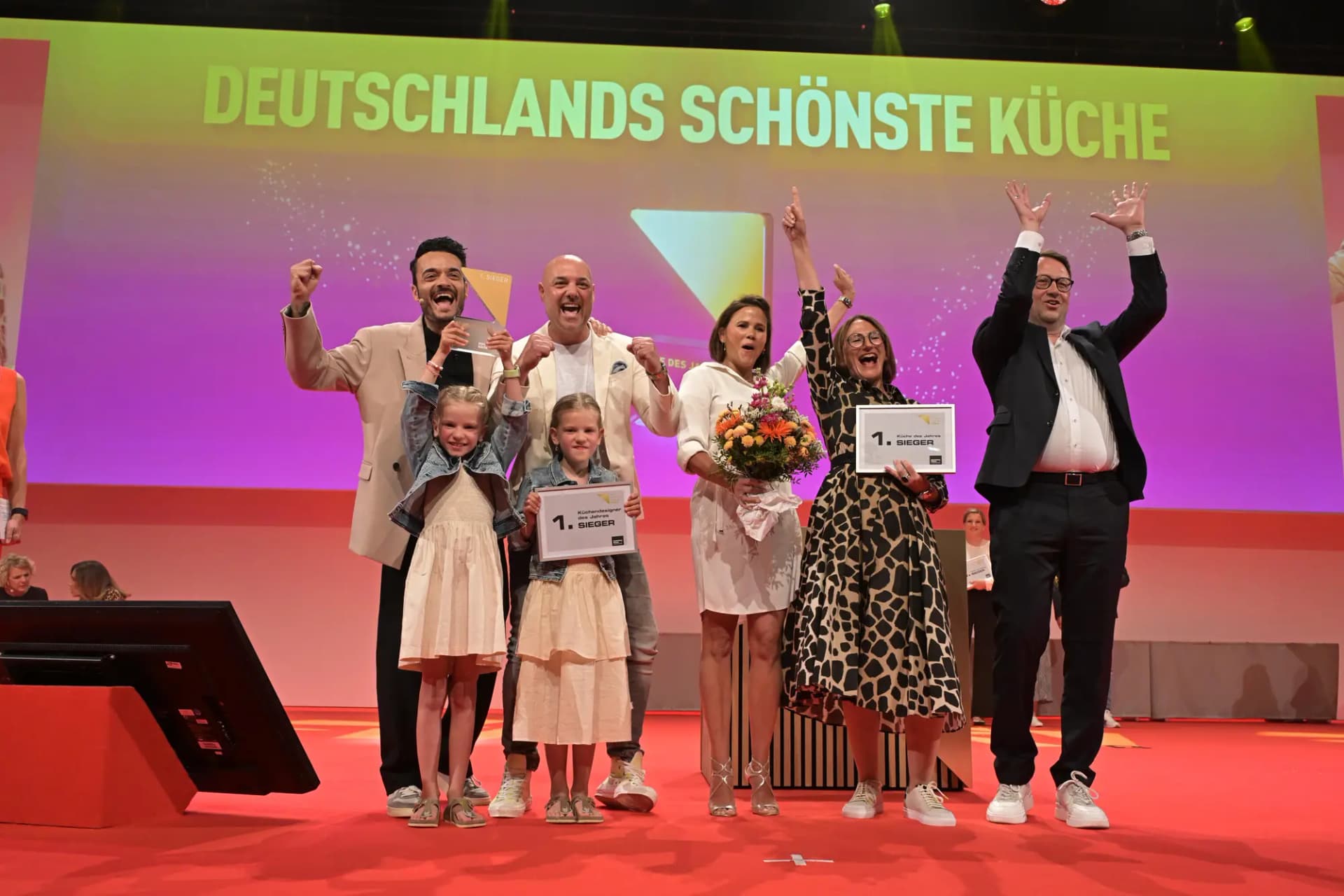 Preisverleihung „Das Goldene Dreieck 2024“: die Kundenfamilie mit der Urkunde „Schönste Küche des Jahres“ auf der Bühne, dahinter der Schriftzug „Deutschlands schönste Küche“