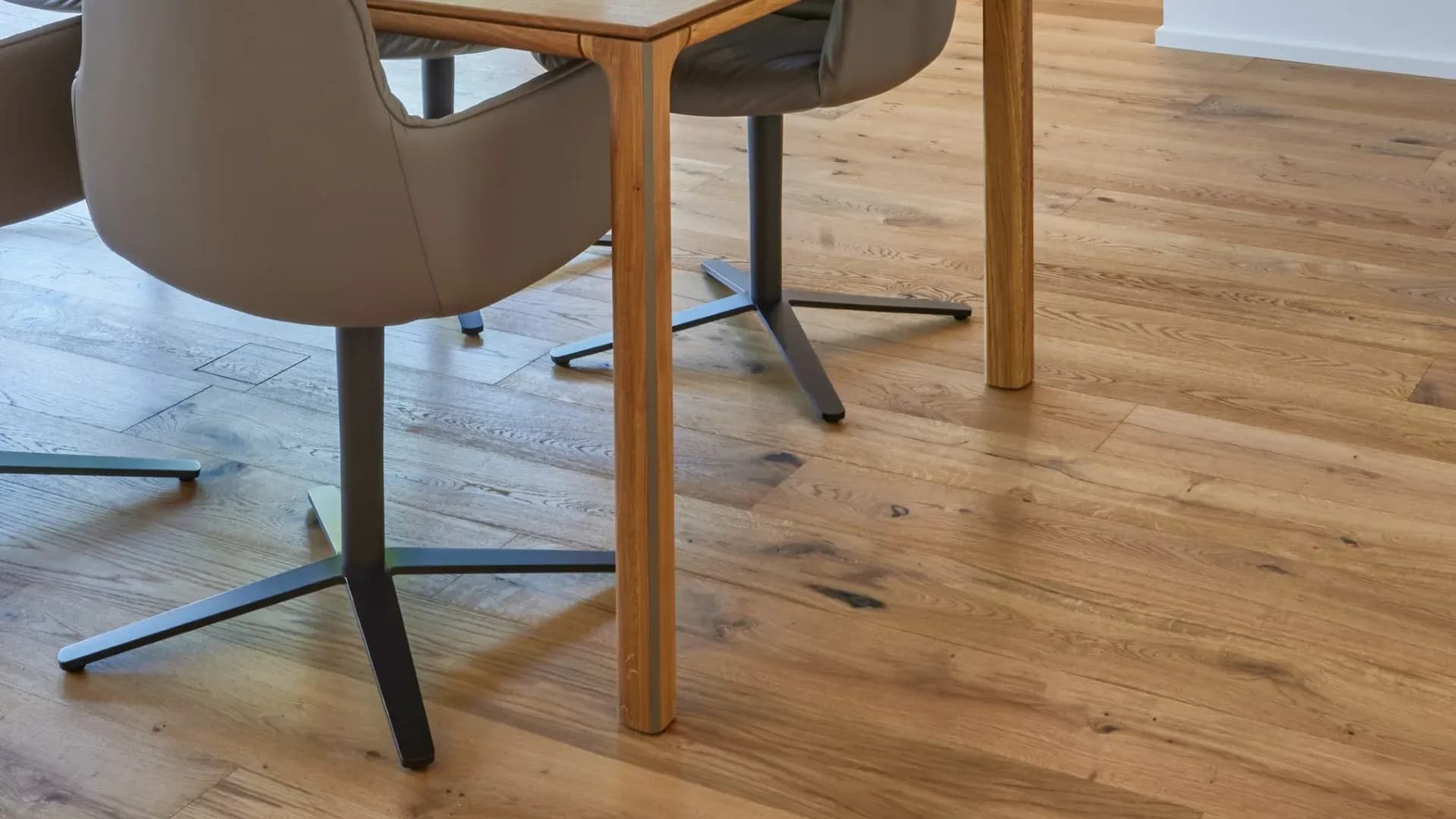 Geölte Eichendielen mit lebhafter Maserung unter einem Esstisch aus Holz und zwei Lederstühlen