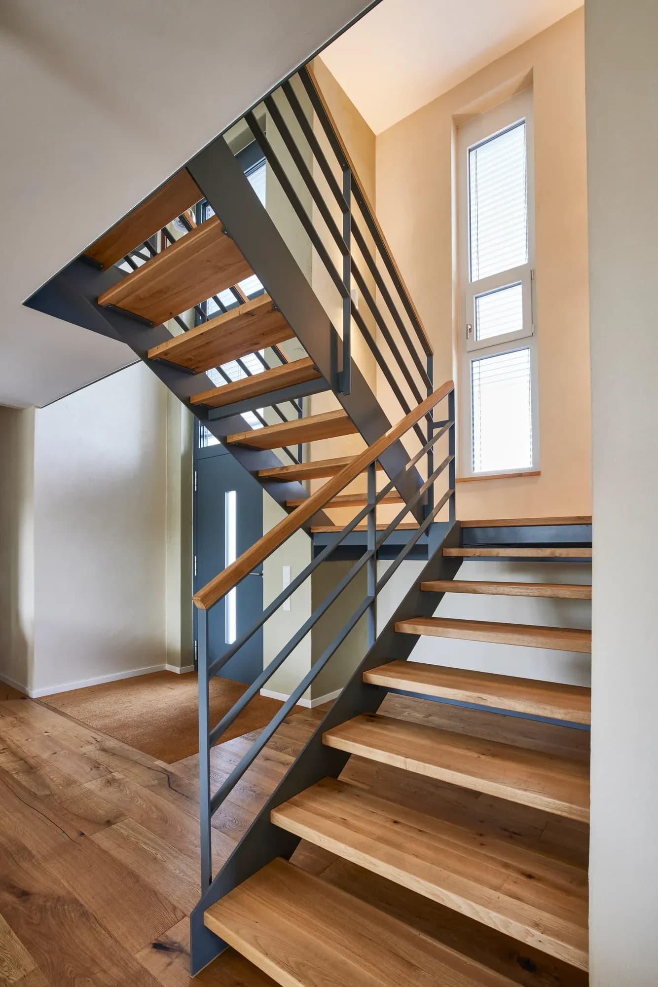Offene Treppe aus schwarzem Flachstahl mit Eichenstufen am Fenster.
