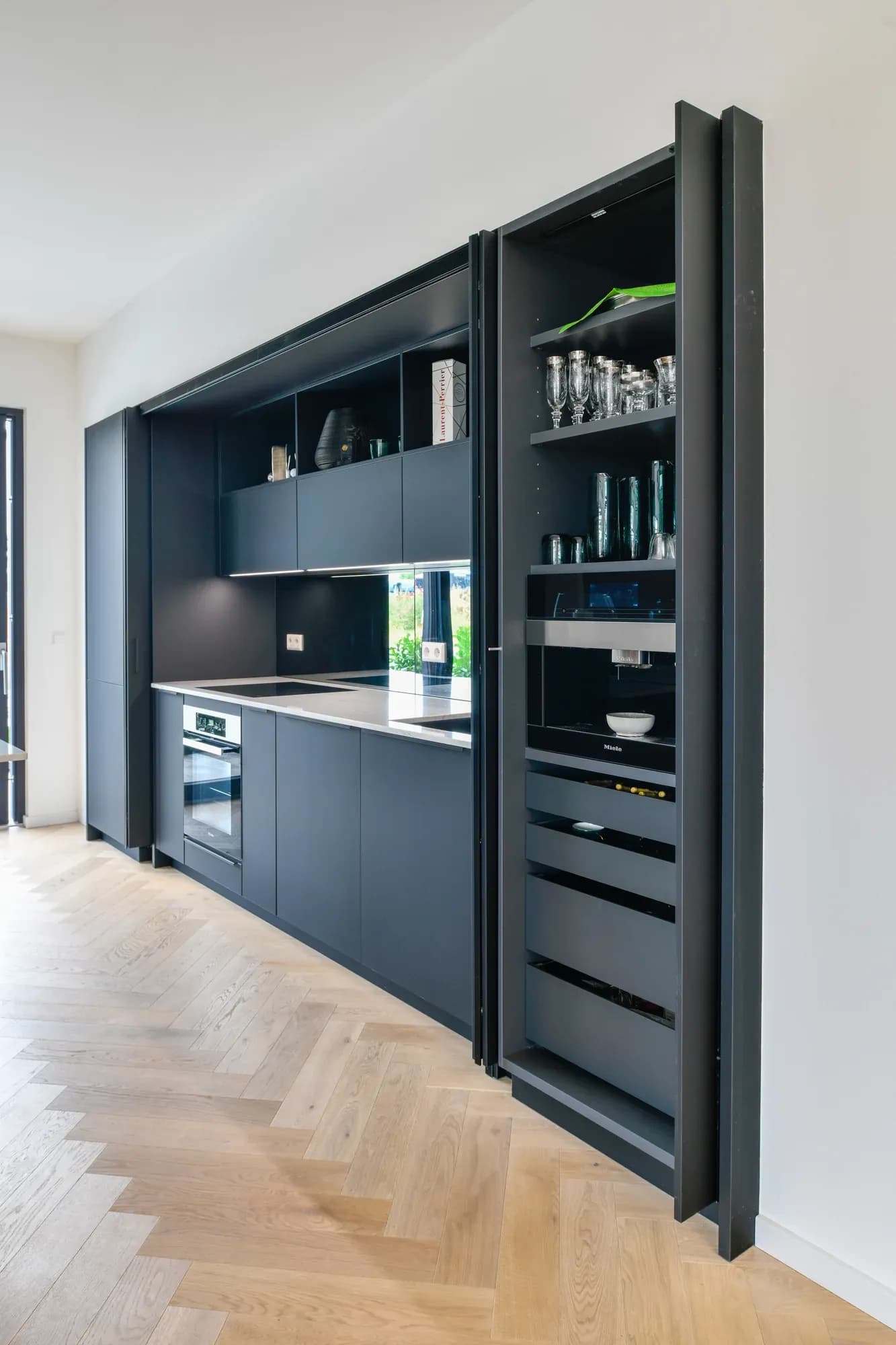 Vollintegrierte Küchenzeile in Anthrazit mit geöffnetem Pocket-Door-Vorratsschrank: Gläser, Miele-Vollautomat und Auszüge.
