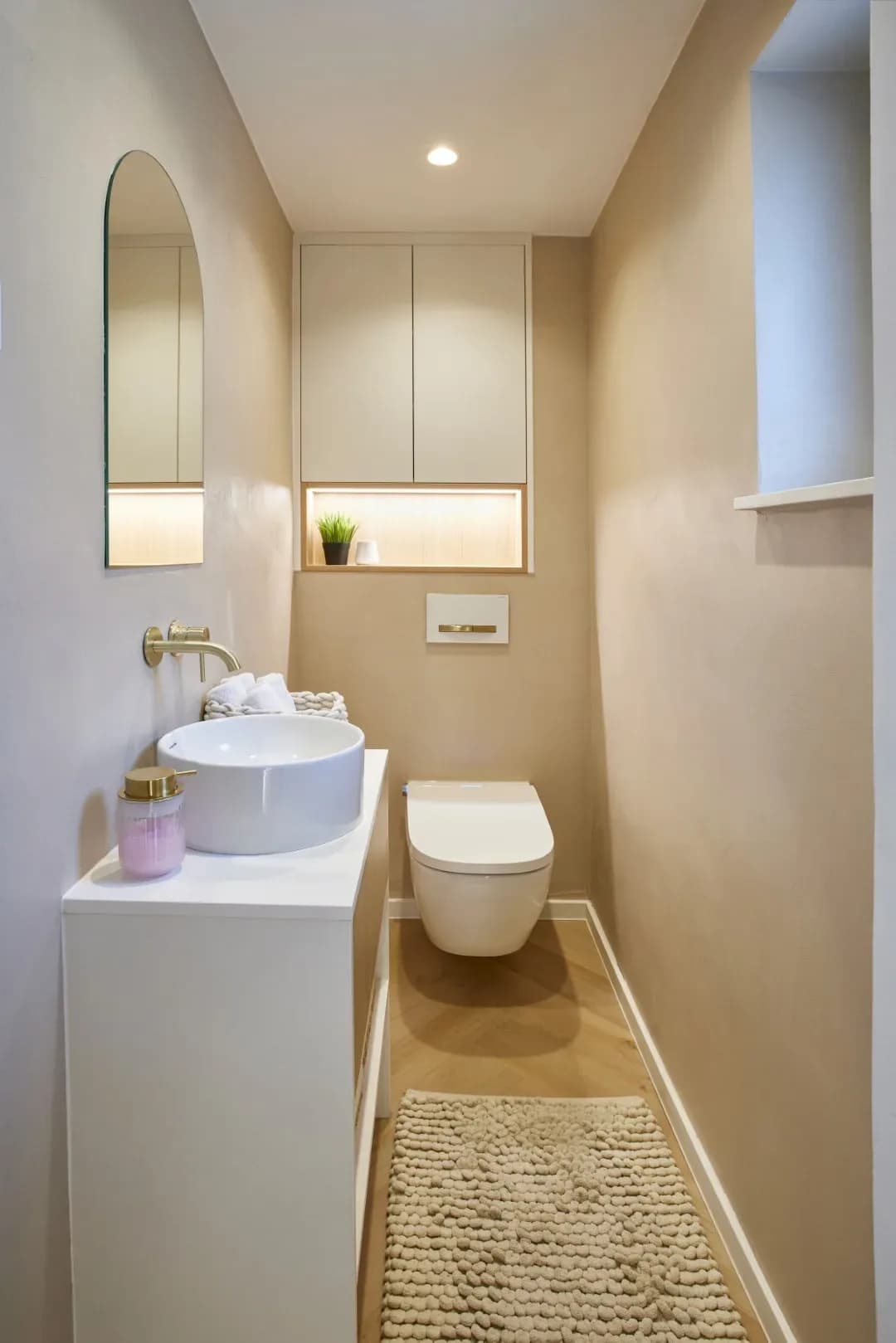 Gäste-WC mit weißem Waschtisch, Messingarmatur und beleuchteter Holznische, Boden aus Eichen-Fischgrätparkett