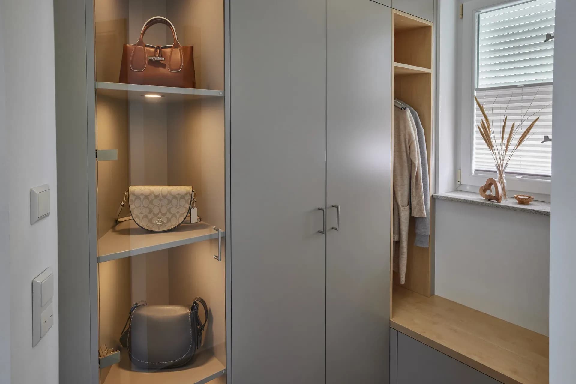 Maßgefertigte Garderobe mit beleuchteten Glasfächern für Handtaschen, grauen Schranktüren und offener Nische in Eiche